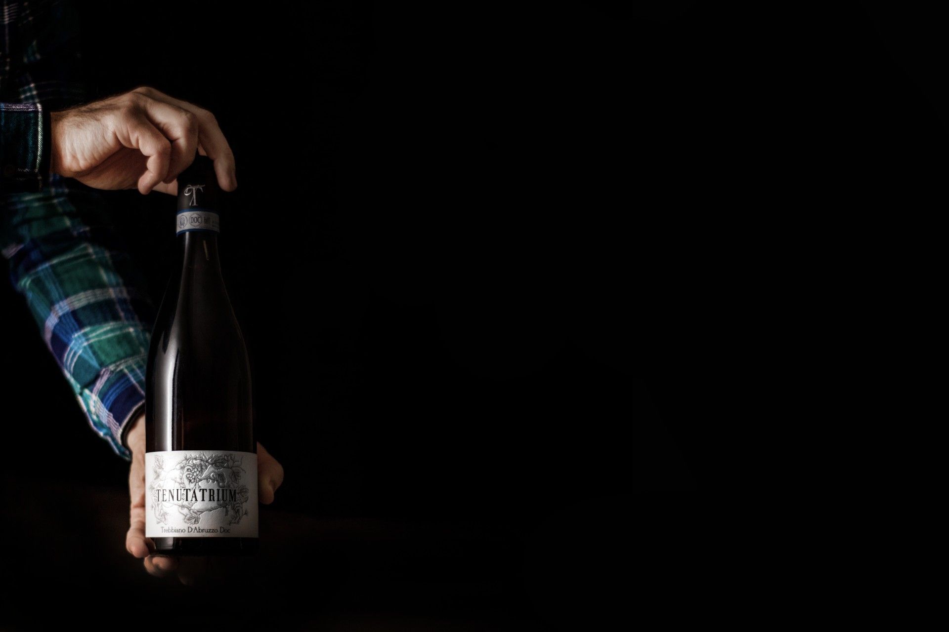 mani ragazzo tengono in mano una bottiglia di Trebbiano D'Abruzzo DOC della Tenuta Trium di Notaresco a Teramo